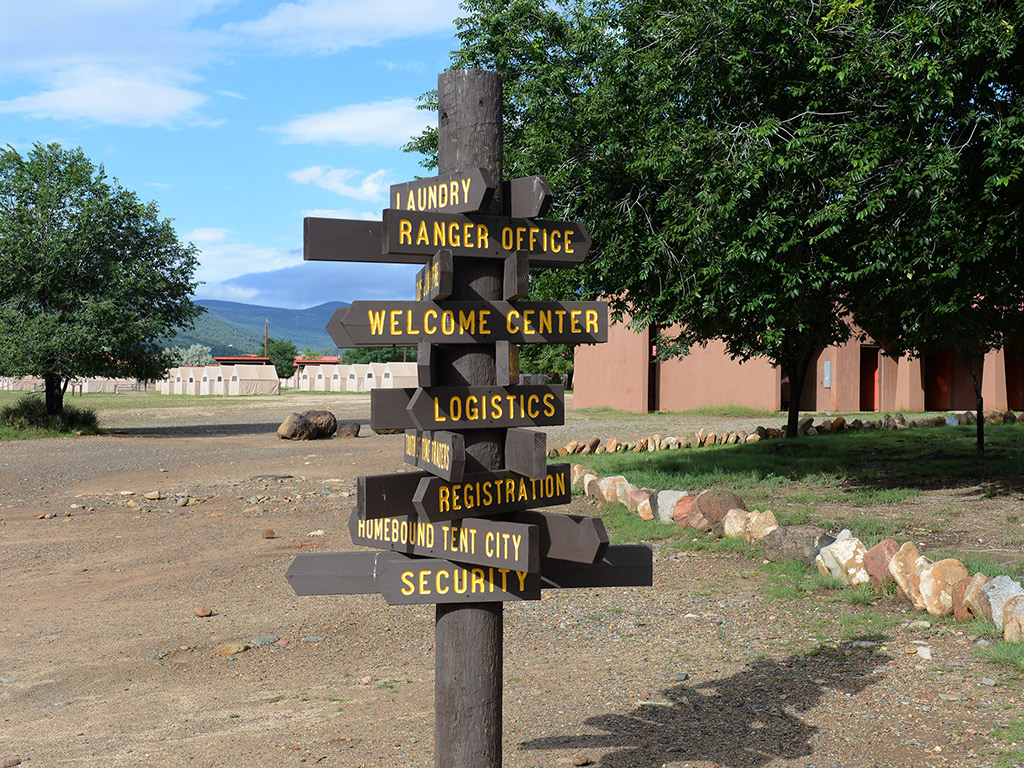 A wood sign outside with several directional labels including where to go to find the ranger office, welcome center and more.